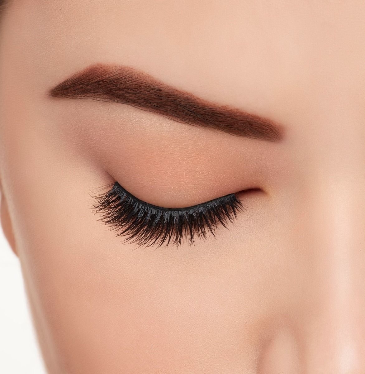 : A model with one eye open wearing Ardell Aqua Lashes 340 upper false lashes to show how they look on the eye